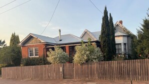 A two-story brick house with a wooden fence, a dog on a leash, and a clear sky.