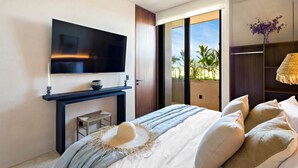 Une chambre moderne avec un grand lit, un téléviseur à écran plat fixé sur une console sombre, un petit tabouret et une vue sur l’extérieur grâce à une porte coulissante.