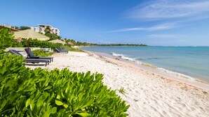 Une plage avec des chaises longues, un bâtiment doté d’un balcon et un ciel bleu azur.