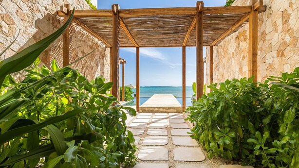 Un chemin de pierre mène à une pergola en bois d’où l’on peut admirer la mer.