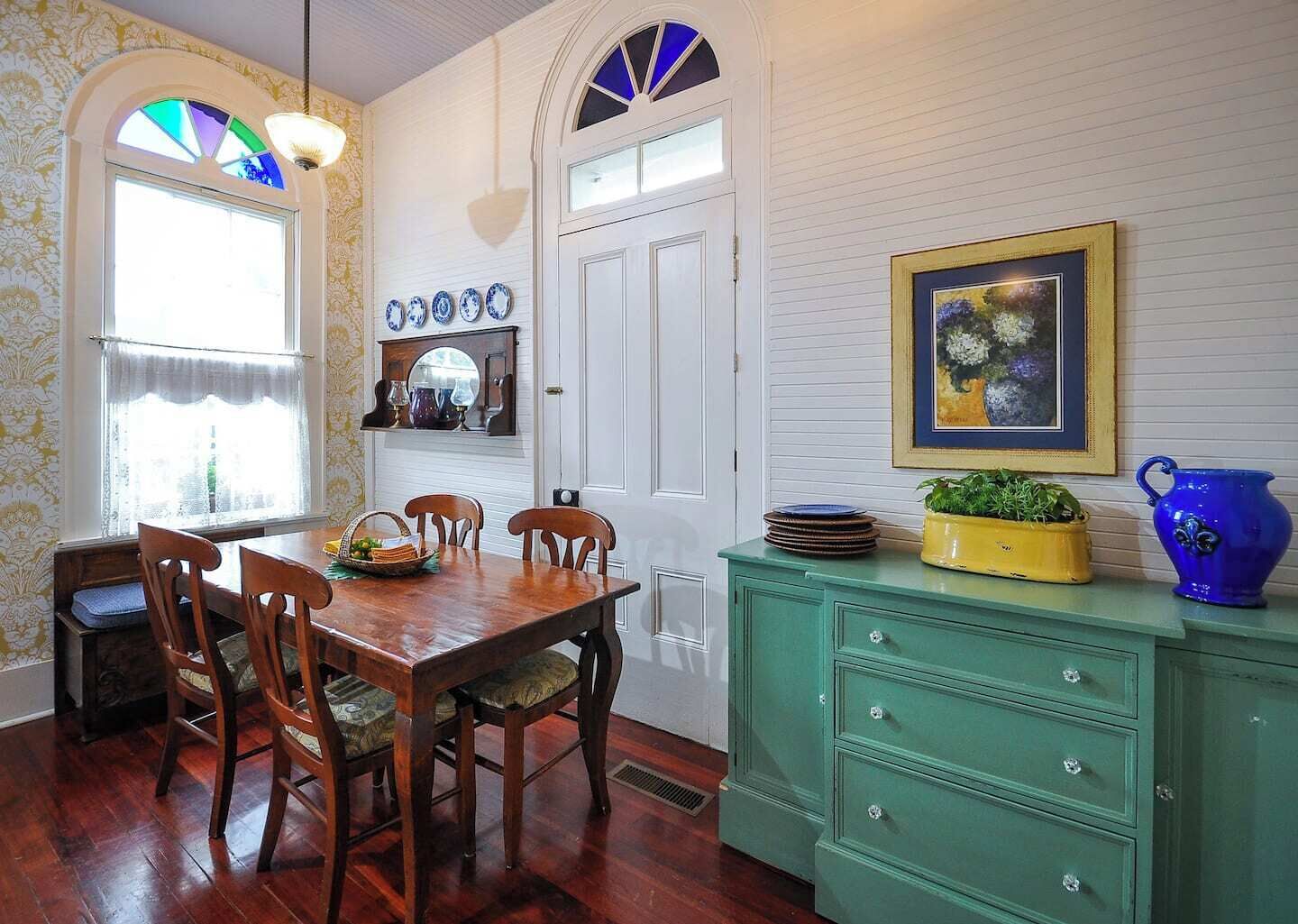 Un comedor con una mesa y sillas de madera, un mueble verde y un ventanal con vidrieras.