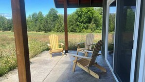 Un patio couvert avec deux fauteuils Adirondack et une porte vitrée donnant accès à une véranda.