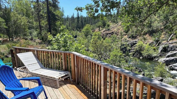 Une terrasse en bois avec des chaises longues et une vue sur une rivière et une forêt.