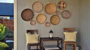Un espace patio avec une table en bois et deux chaises, un panier décoratif fixé au mur et une petite plante en pot.