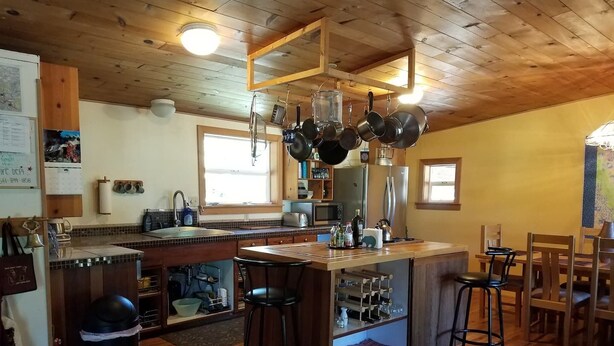A kitchen with wooden cabinets, a central island with stools, a refrigerator, and a window. - Ruch Refuge in Jacksonville (Jacksonville)