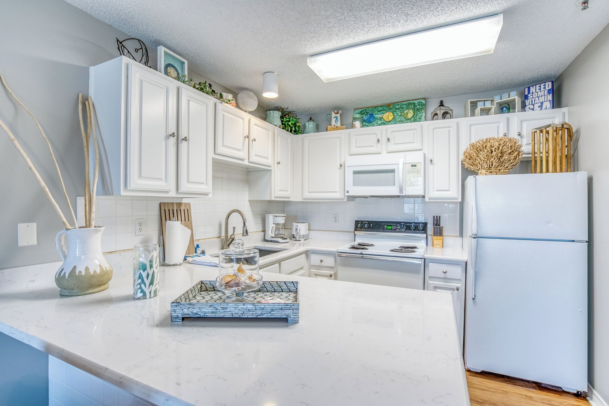 A modern kitchen with white cabinets, a white refrigerator, a microwave, and a coffee maker.