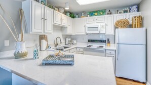Una cocina moderna con armarios blancos, un refrigerador blanco, un microondas y una cafetera.