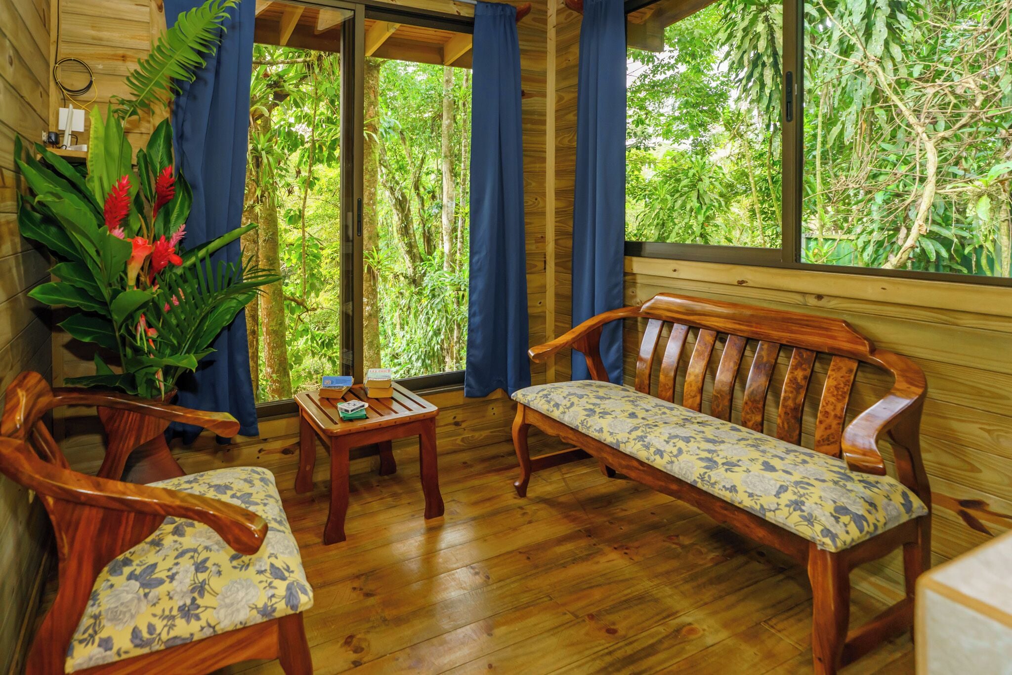 Une pièce en bois avec un banc, deux chaises, une petite table et une grande fenêtre donnant sur un paysage verdoyant.