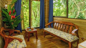 Une pièce en bois avec un banc, deux chaises, une petite table et une grande fenêtre donnant sur un paysage verdoyant.