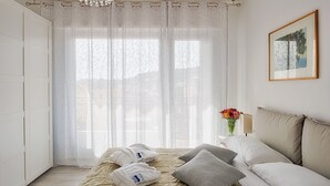 Una camera da letto ordinata con un letto, cuscini, un comodino con un vaso di fiori e un quadro appeso al muro.