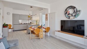 Un soggiorno moderno con divano, un'area pranzo con tavolo e sedie, una cucina con forno integrato e una libreria.