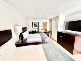 Habitación de hotel con dos camas, televisión, escritorio y armario.