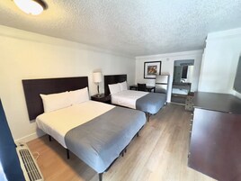 Habitación de hotel con dos camas, un escritorio, una silla, una lámpara y un armario.