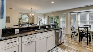 A modern kitchen with white cabinets, a black countertop, stainless steel appliances, and a chandelier. - Spacious 4BR home in Sea Pines, Hilton Head Island, sleeps 10 comfortably. (Hilton Head Island)