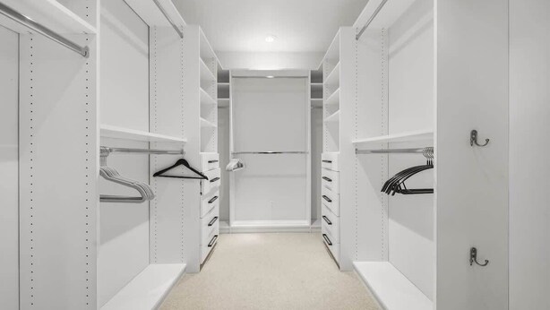 Un vestidor estrecho con estantes blancos y espacio para colgar.