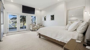 Un dormitorio con una cama grande, una zona de estar con sillas y vistas a través de un ventanal.