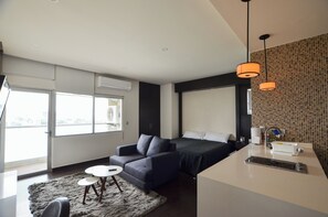 Ein modernes Hotelzimmer mit Sofa, kleinem Tisch, Bett und Küchenzeile.
