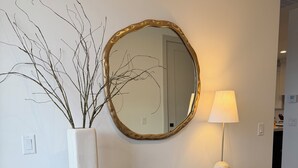 A black console table with a gold-framed mirror above it, a white vase with branches, a small bowl, and a lamp. Two wicker baskets are placed under the table. - Sol Haven Washington, Utah (Washington)