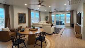 A spacious living room with a round dining table, sofas, and a large window offering a city view. - Sol Haven Washington, Utah (Washington)