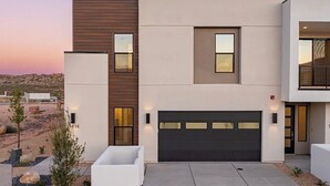 A modern two-story house with a garage, a flat roof, and a desert landscape in the background. - Sol Haven Washington, Utah (Washington)
