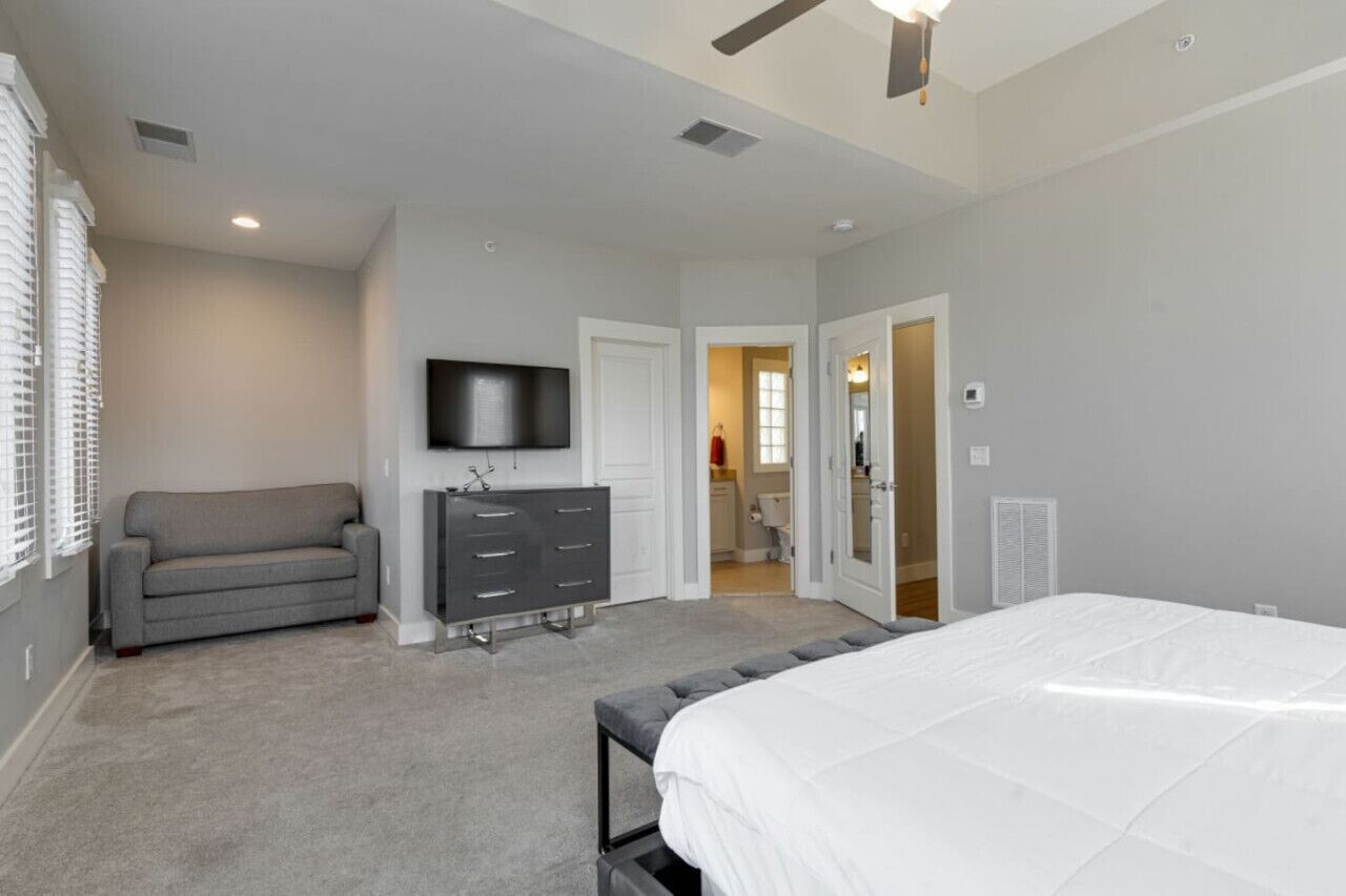 Une chambre à coucher comprenant un lit, une commode, un téléviseur et une porte donnant sur une salle de bain.