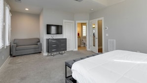 Une chambre à coucher comprenant un lit, une commode, un téléviseur et une porte donnant sur une salle de bain.