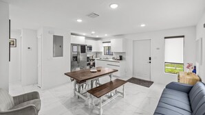 A modern kitchen with white cabinets, a dining table with benches, a gray sofa, and a small wooden side table. - Urban Sabor - Modern Miami - King Beds - Fenced Yard - Parking (Miami)