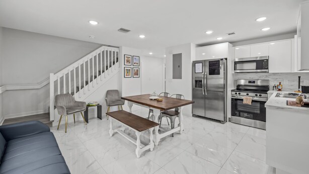 A modern kitchen with white cabinetry, stainless steel appliances, a wooden dining table, and a bench. - Urban Sabor - Modern Miami - King Beds - Fenced Yard - Parking (Miami)