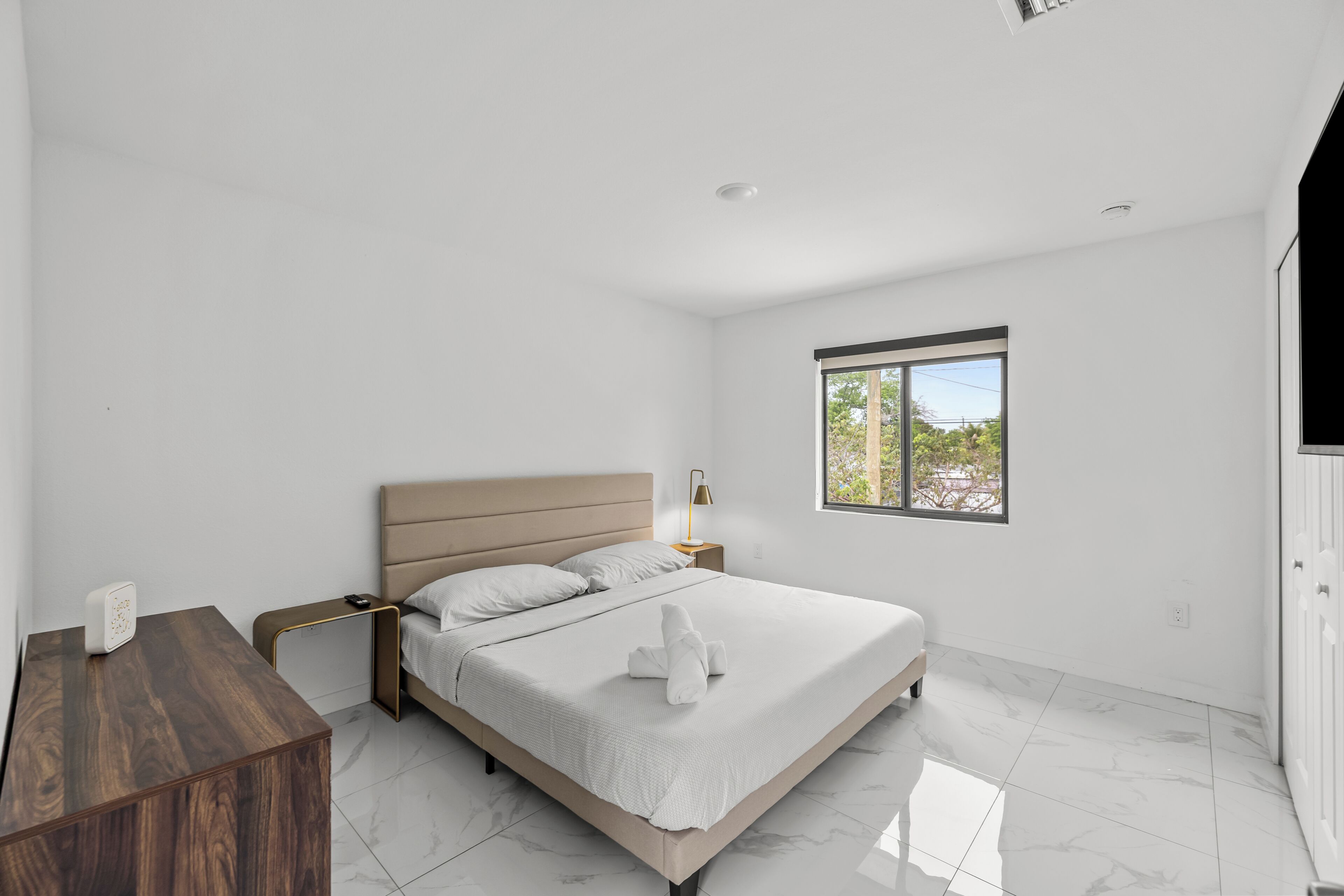 Quarto com cama, mesa de cabeceira, abajur e janela com vista.