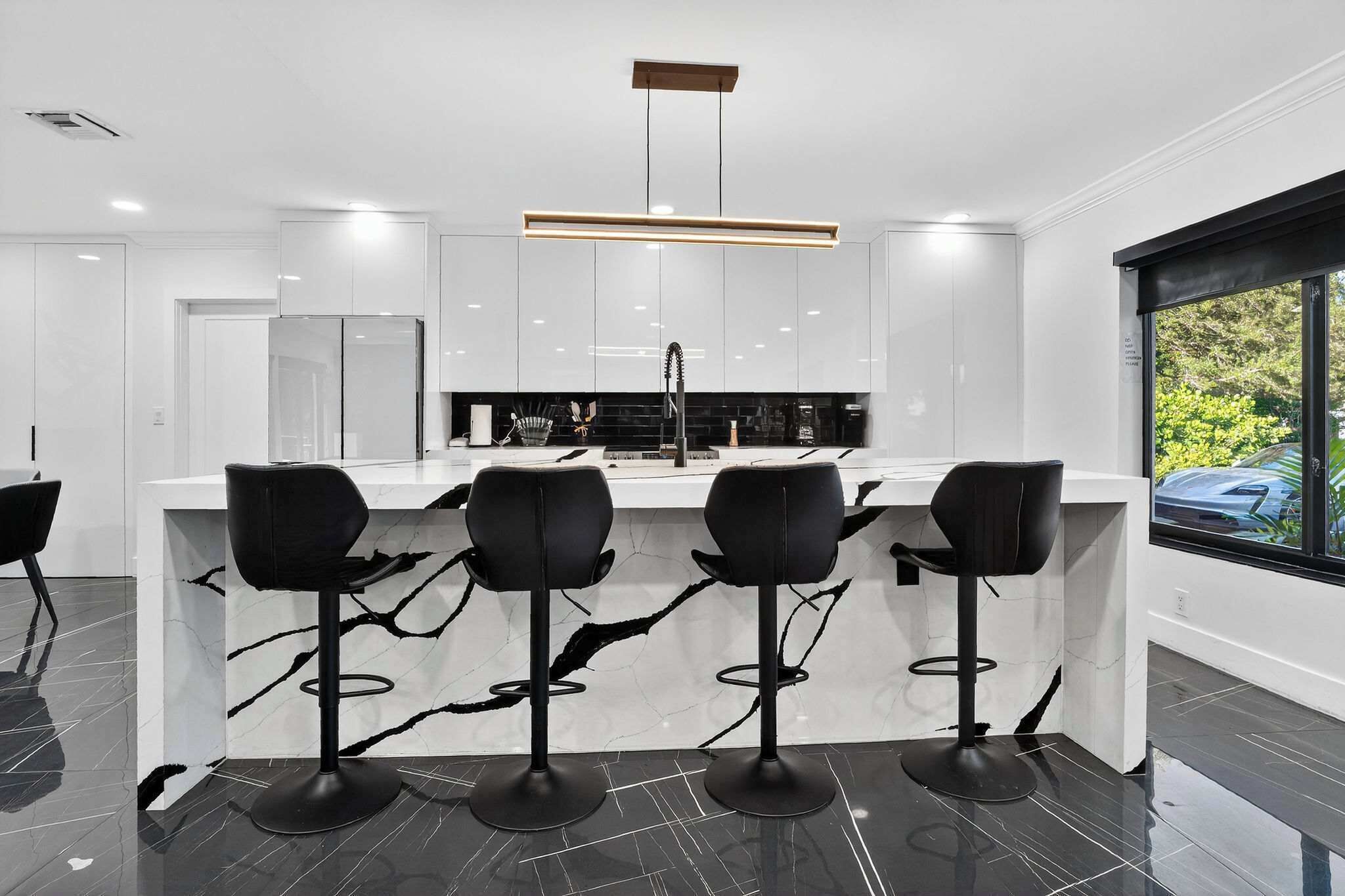 A modern kitchen with three black bar stools, a central island, and a large window.