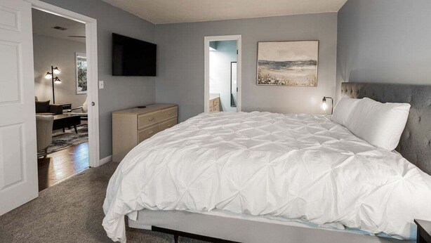 Een slaapkamer met een groot bed, een dressoir, een flatscreen televisie aan de muur en een schilderij boven het bed.