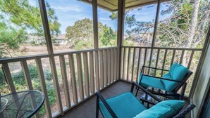 Een overdekt balkon met een tafel en twee stoelen, met uitzicht op bomen en een huis in de verte.
