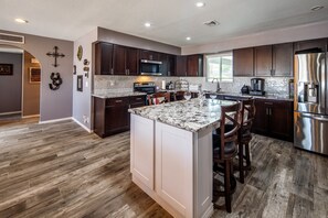 A modern kitchen with dark wood cabinets, a granite countertop, stainless steel appliances, and a large island with bar stools. - Coral Havasu Vacation (Lake Havasu City)