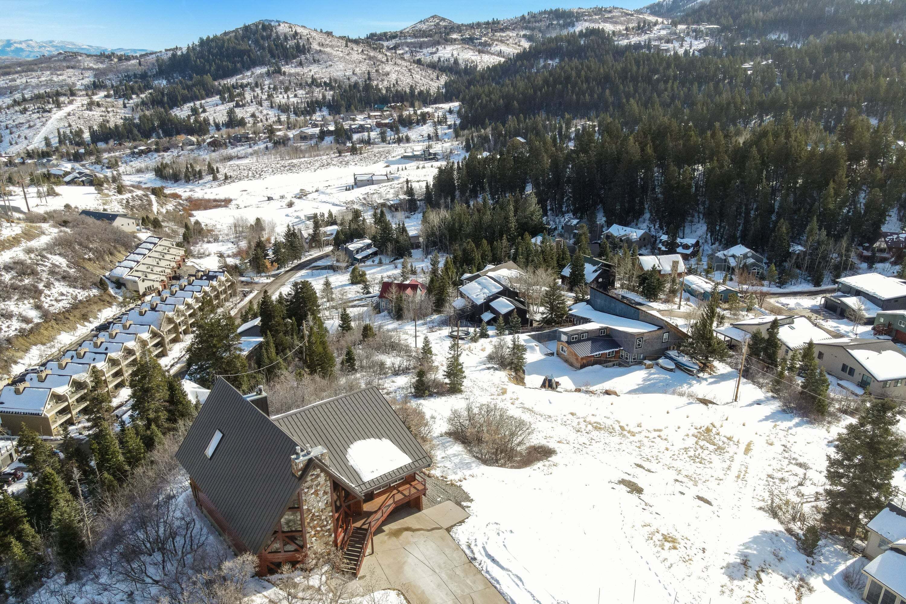 Un chalet doté d’une cheminée imposante, entouré d’un paysage enneigé et d’une forêt dense.
