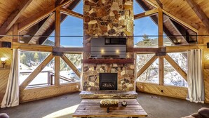 A spacious room with a stone fireplace, large windows, and wooden beams. - Cozy Rustic Escape (Park City)