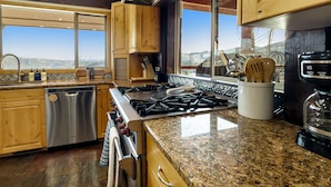 A modern kitchen with wooden cabinets, stainless steel appliances, and a large window offering a view of the landscape. - Cozy Rustic Escape (Park City)