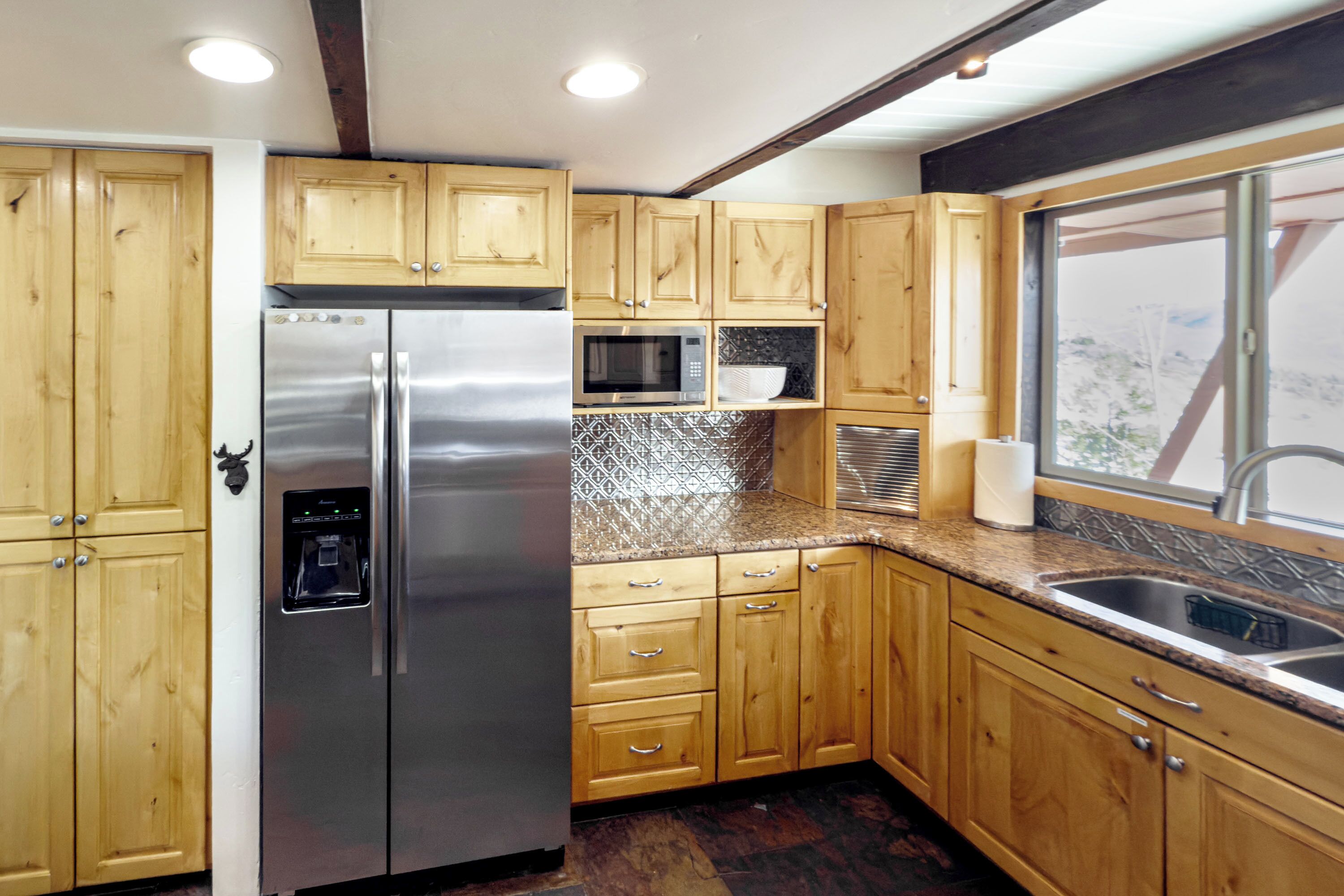 A compact kitchen with wooden cabinets, stainless steel appliances, and a window providing a view.