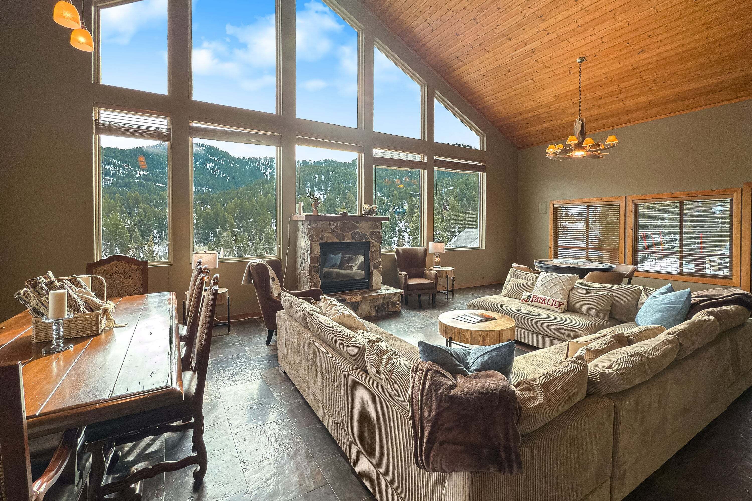 A spacious living room with a large window, a stone fireplace, a wooden ceiling, and a cozy seating area.