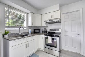 A modern kitchen with white cabinets, a stainless steel oven, a microwave, and a sink.