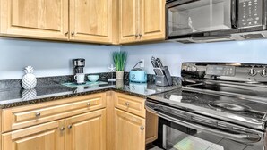 A kitchen with wooden cabinets, a stainless steel stove, a microwave, a toaster, and a coffee maker. - Coastside (Santa Rosa Beach)