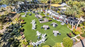 An outdoor seating area with tables and chairs, surrounded by lush greenery and palm trees. - Coastside (Santa Rosa Beach)