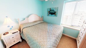 Une chambre à coucher avec un lit, une table de chevet, une lampe, un tableau et une fenêtre avec des stores.