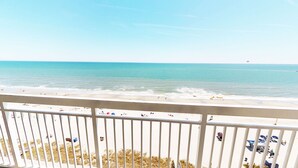 Une vue sur la plage depuis un balcon doté d’une balustrade, avec une plage de sable et l’océan en toile de fond.