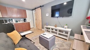 A modern living room with a grey sofa, ottoman, and a patterned rug. A flat-screen TV is mounted on the wall, and a white console table is against the wall. - Cute & Cozy Renovated APT in the Heart of Phoenix (Phoenix)