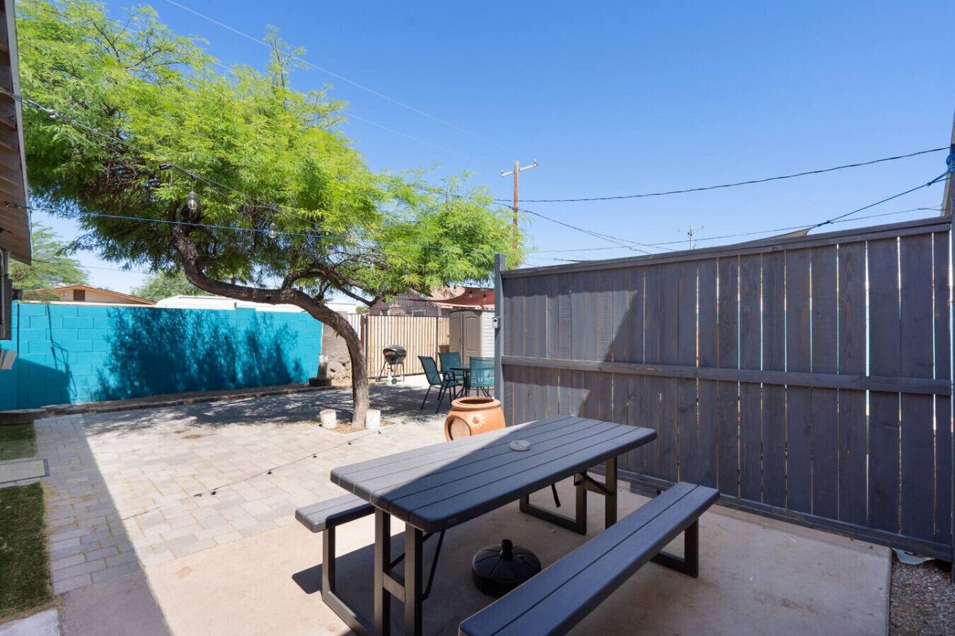 A backyard with a picnic table, a barbecue grill, and a fenced area.