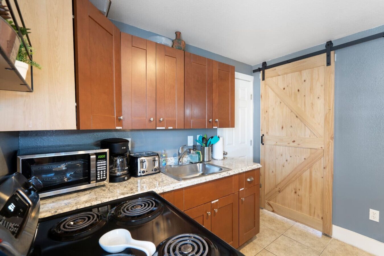 A compact kitchen with wooden cabinets, a microwave, a coffee maker, a toaster, and a stove.