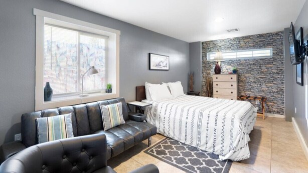 A modern bedroom with a bed, a sofa, a desk, and a stone accent wall. - Cute & Cozy Renovated APT in the Heart of Phoenix (Phoenix)