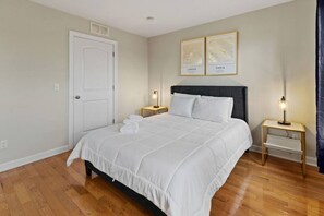 Une chambre à coucher bien rangée, avec un grand lit, deux tables de chevet avec des lampes, une porte et deux cartes encadrées accrochées au mur.