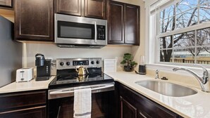 A modern kitchen with dark wood cabinets, a stainless steel microwave, a gas stove, a sink, and a window with a view of trees. - Cozy and Comfortable 1-br in the Heart of Detroit (Detroit)