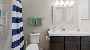 A bathroom with a striped shower curtain, a toilet, a sink with toiletries, and a mirror. - Cozy and Comfortable 1-br in the Heart of Detroit (Detroit)